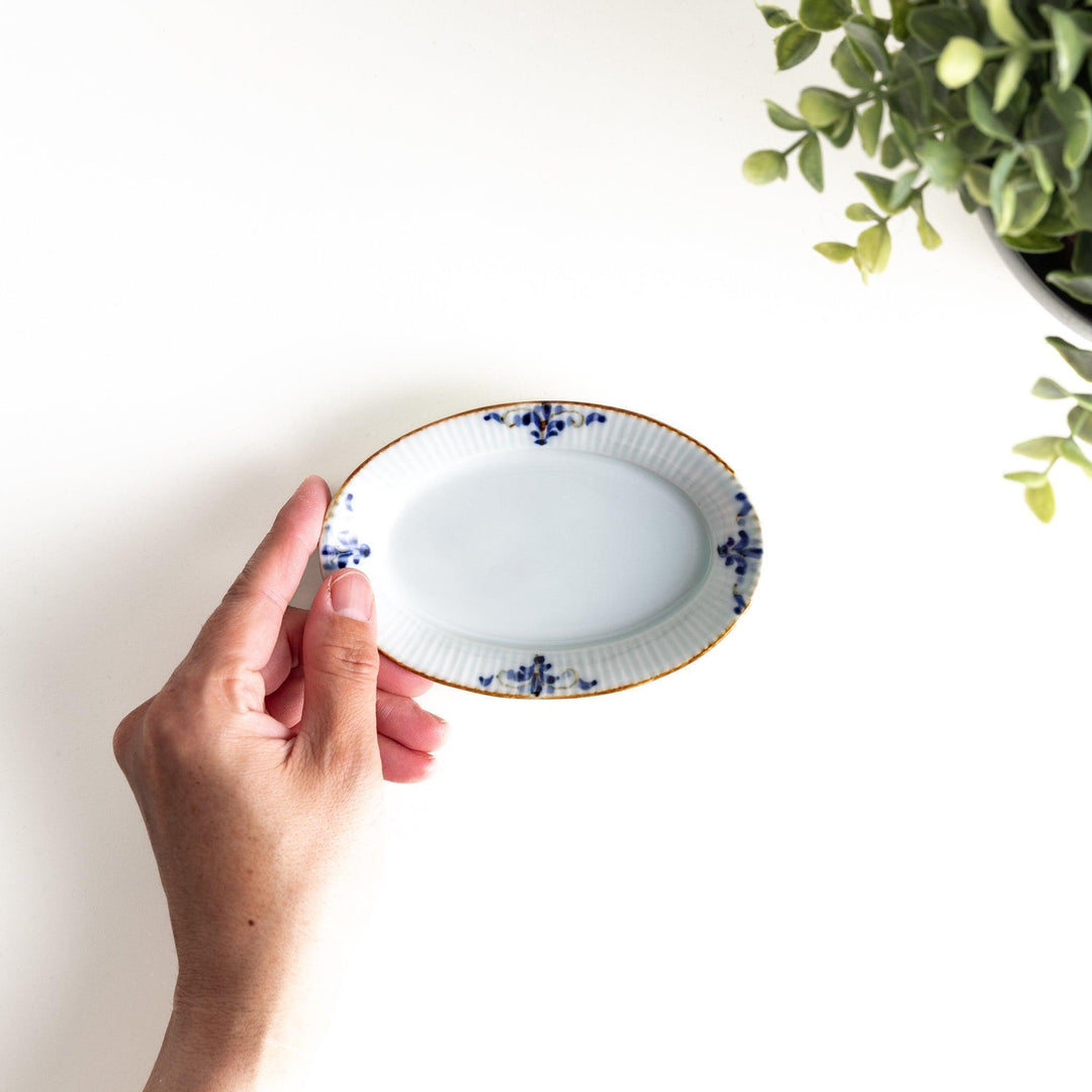 An oval sauce dish featuring blue floral motifs and a ribbed design around the edges with brown accent trim.