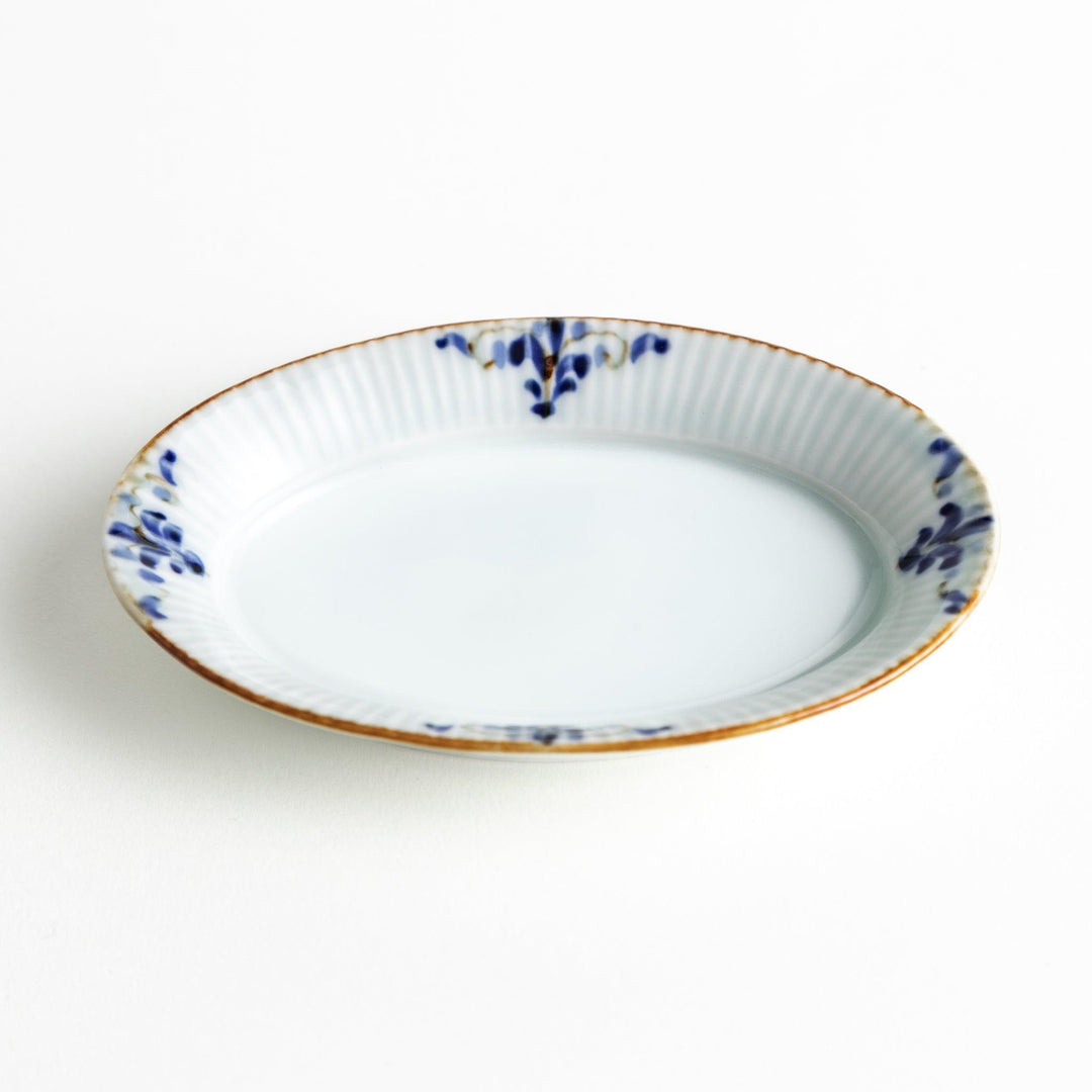 An oval sauce dish featuring blue floral motifs and a ribbed design around the edges with brown accent trim.