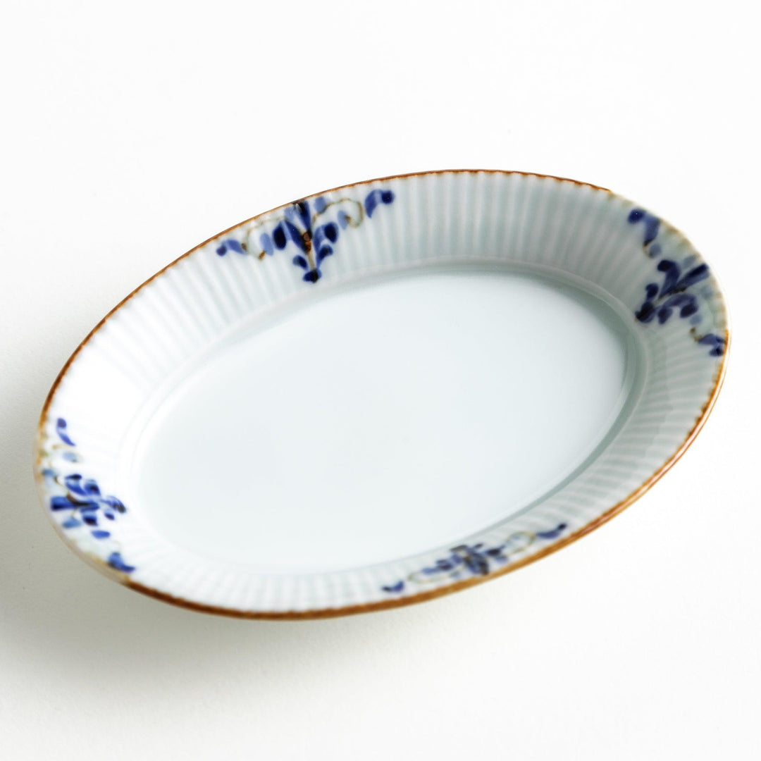 An oval sauce dish featuring blue floral motifs and a ribbed design around the edges with brown accent trim.