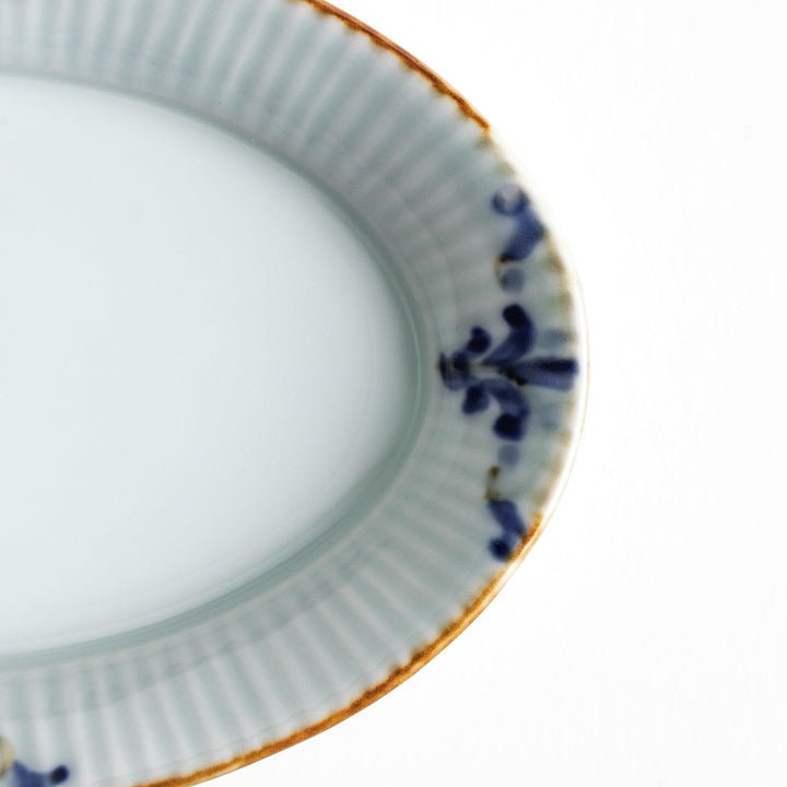 An oval sauce dish featuring blue floral motifs and a ribbed design around the edges with brown accent trim.