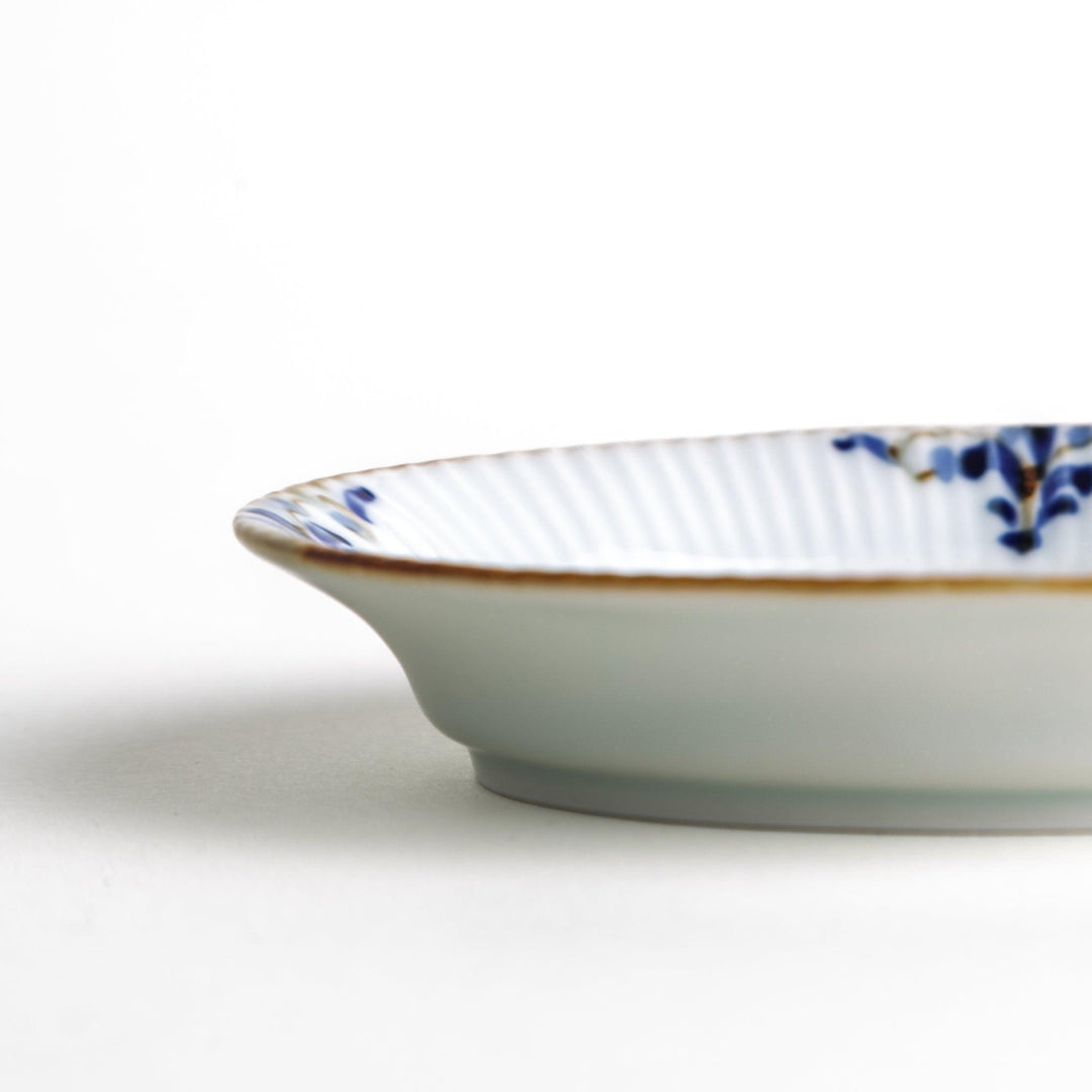 An oval sauce dish featuring blue floral motifs and a ribbed design around the edges with brown accent trim.