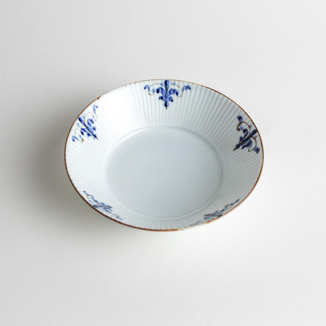 A round, shallow white bowl with blue floral patterns and a ribbed design along the edges and brown accent trim.