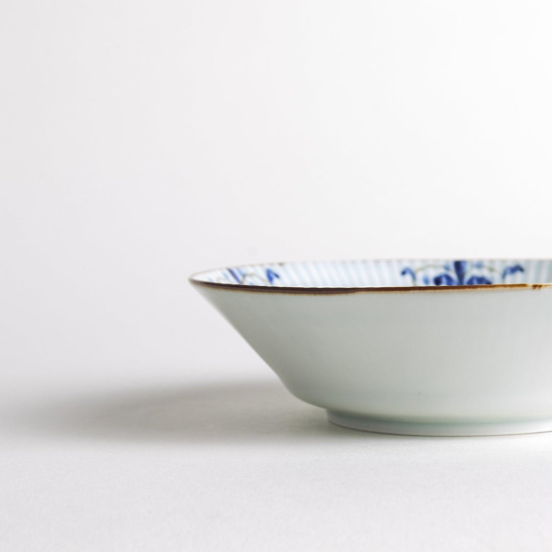 A round, shallow white bowl with blue floral patterns and a ribbed design along the edges and brown accent trim.