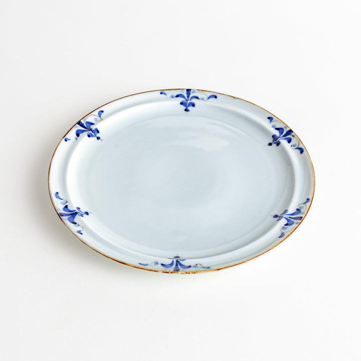 A small porcelain salad plate with a scalloped edge, decorated with blue and white floral motifs and brown accent trim.