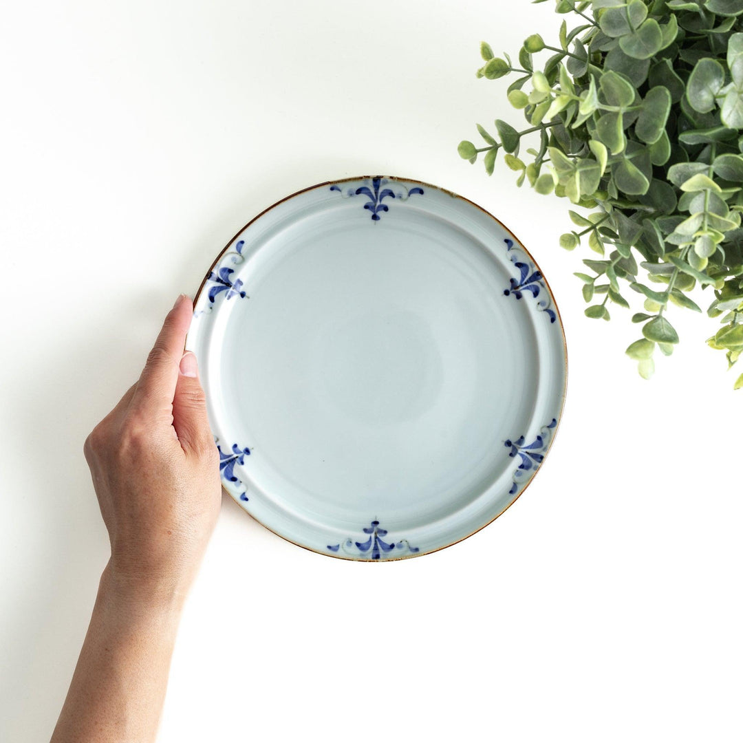 A small porcelain salad plate with a scalloped edge, decorated with blue and white floral motifs and brown accent trim.