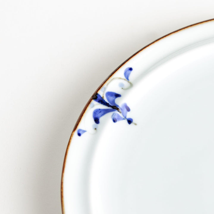 A small porcelain salad plate with a scalloped edge, decorated with blue and white floral motifs and brown accent trim.