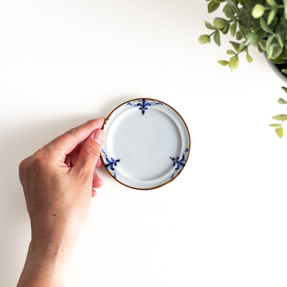 A small porcelain sauce dish with a scalloped edge, featuring a blue and white design of flowers and leaves and brown accent trim.