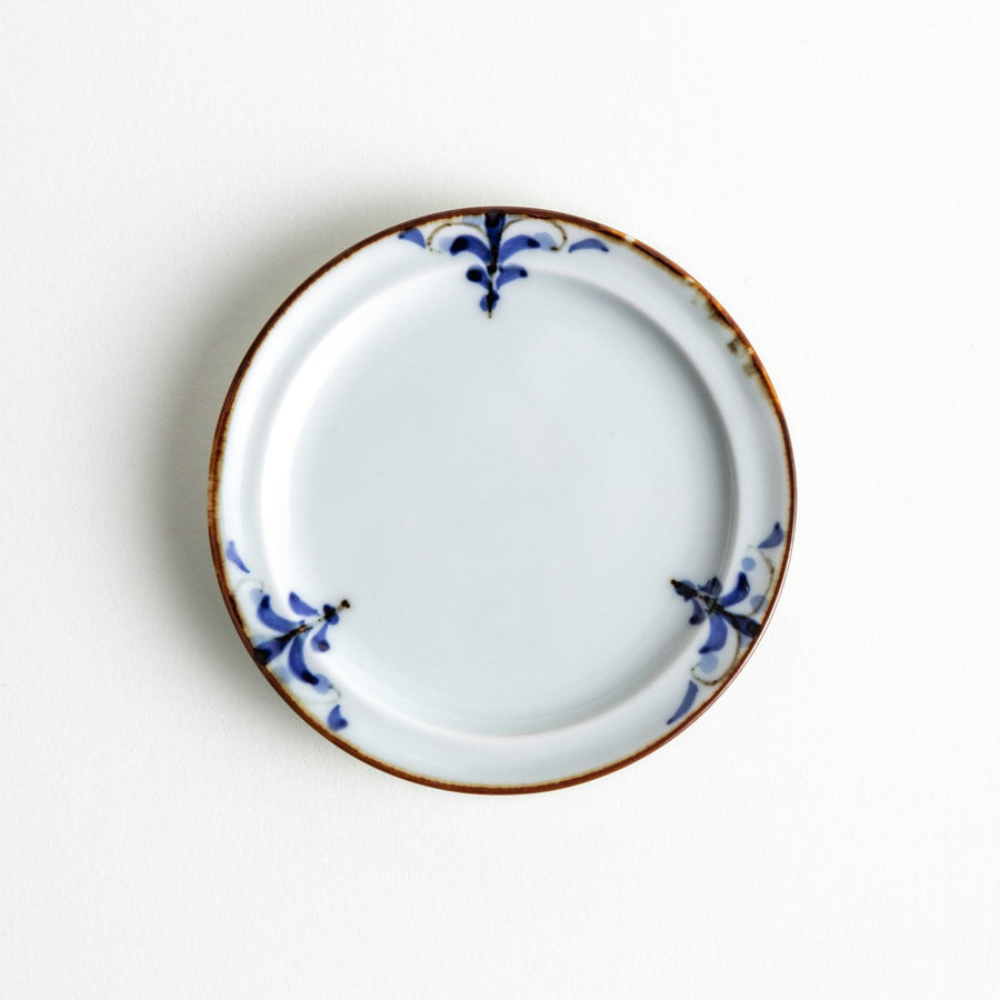 A small porcelain sauce dish with a scalloped edge, featuring a blue and white design of flowers and leaves and brown accent trim.