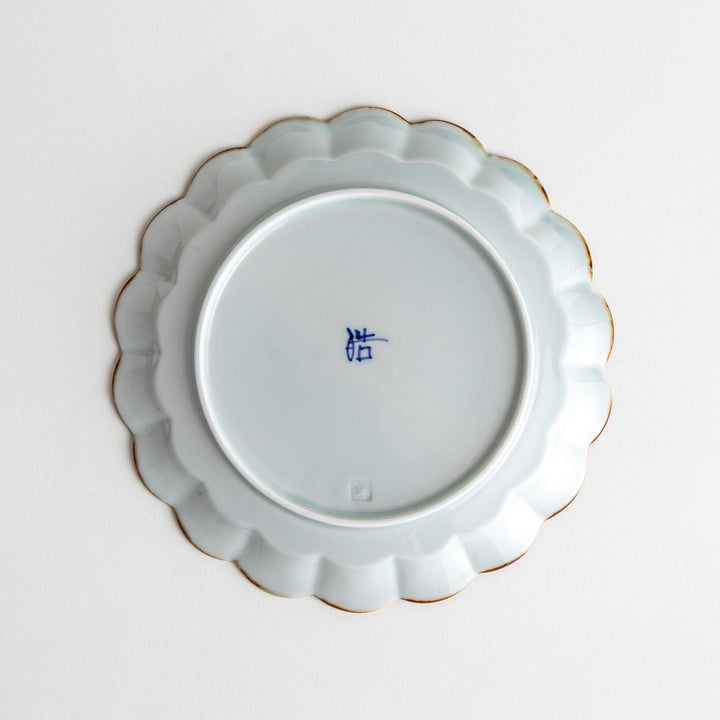 Round white porcelain dessert plate with scalloped edges, adorned with a simple blue floral pattern and brown accent trim.