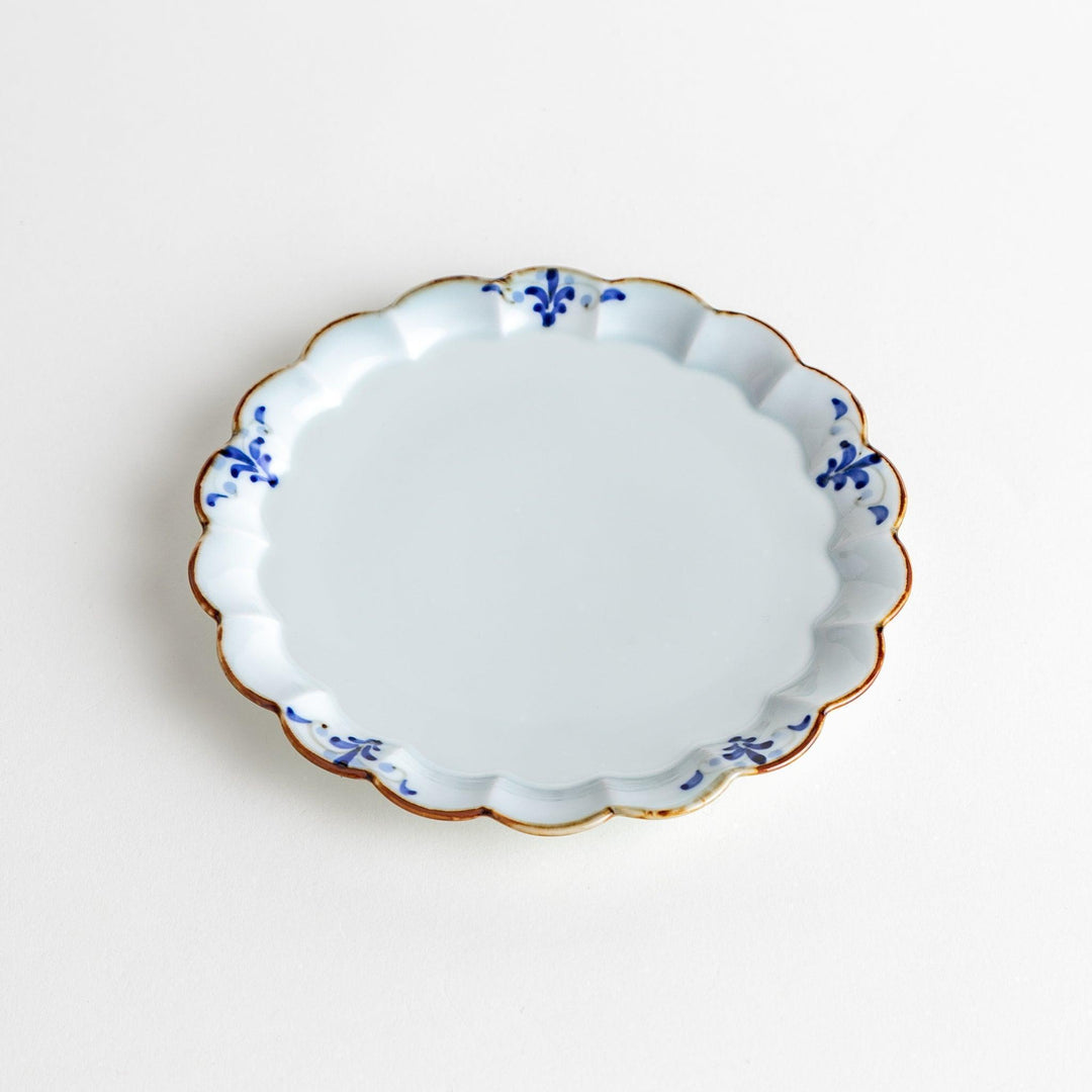 Round white porcelain dessert plate with scalloped edges, adorned with a simple blue floral pattern and brown accent trim.