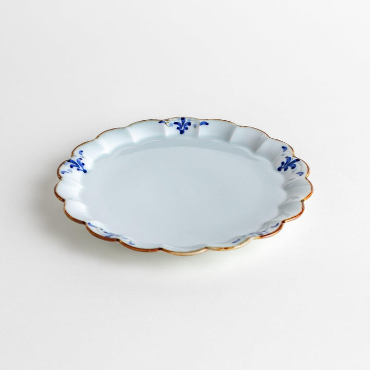 Round white porcelain dessert plate with scalloped edges, adorned with a simple blue floral pattern and brown accent trim.