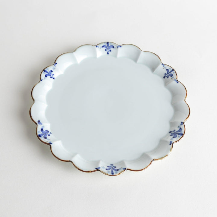 Round white porcelain salad plate with scalloped edges, adorned with a simple blue floral pattern and brown accent trim.