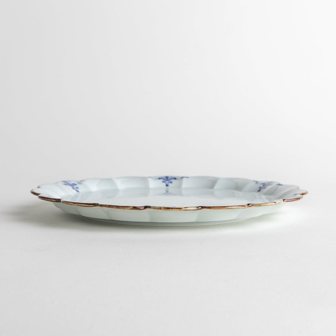 Round white porcelain salad plate with scalloped edges, adorned with a simple blue floral pattern and brown accent trim.