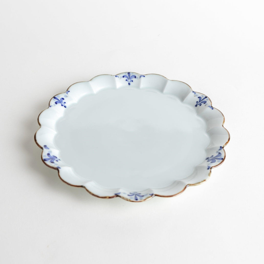 Round white porcelain salad plate with scalloped edges, adorned with a simple blue floral pattern and brown accent trim.