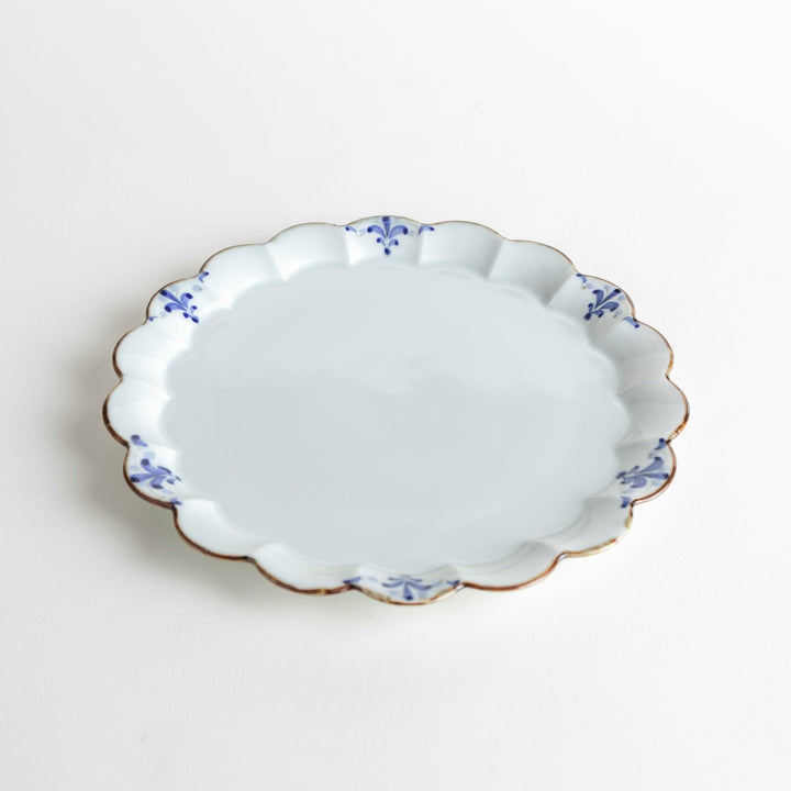 Round white porcelain salad plate with scalloped edges, adorned with a simple blue floral pattern and brown accent trim.