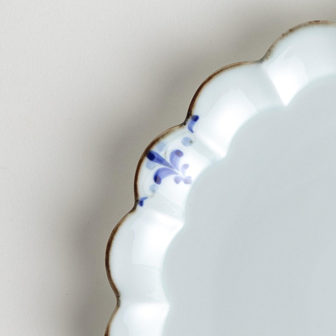 Round white porcelain salad plate with scalloped edges, adorned with a simple blue floral pattern and brown accent trim.