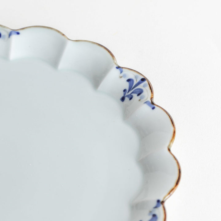 Round white porcelain salad plate with scalloped edges, adorned with a simple blue floral pattern and brown accent trim.