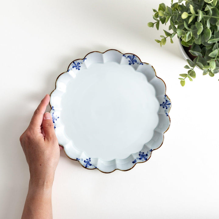 Round white porcelain salad plate with scalloped edges, adorned with a simple blue floral pattern and brown accent trim.