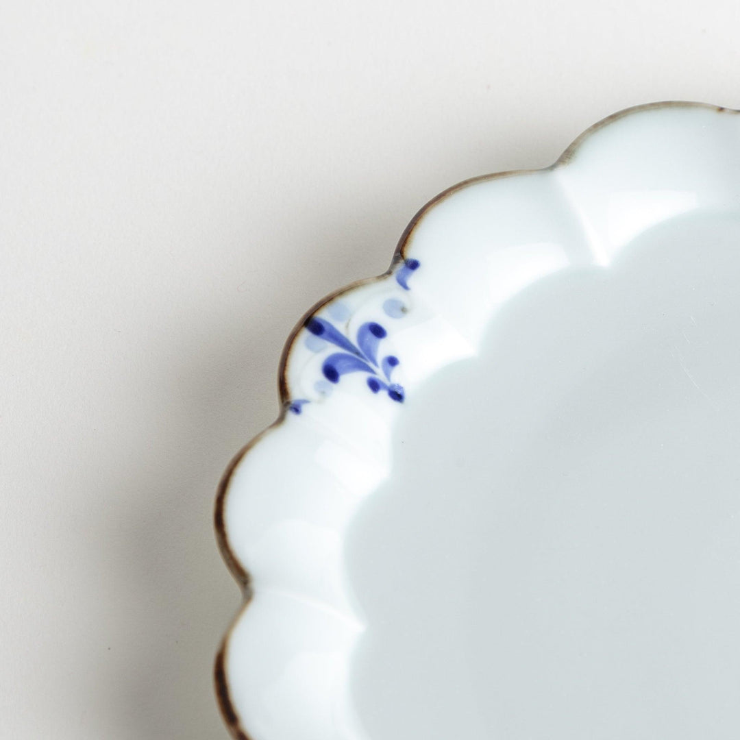 Round white porcelain salad plate with scalloped edges, adorned with a simple blue floral pattern and brown accent trim.