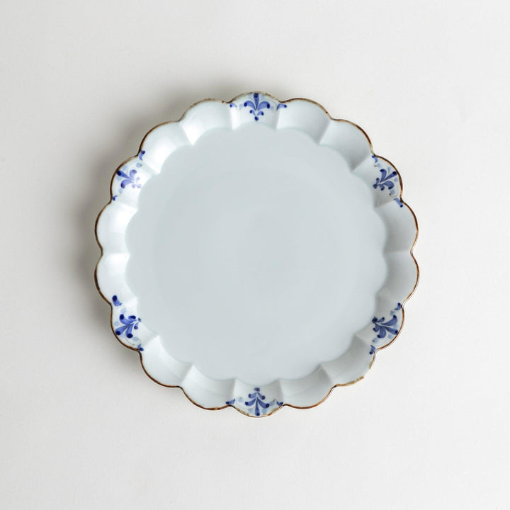 Round white porcelain salad plate with scalloped edges, adorned with a simple blue floral pattern and brown accent trim.