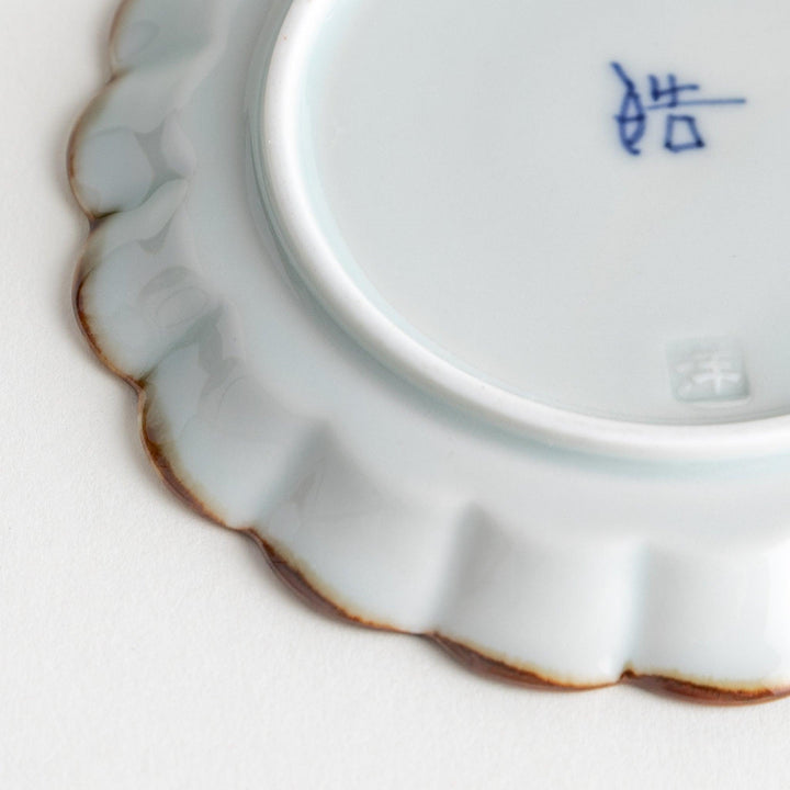 Round white porcelain sauce dish with scalloped edges, adorned with a simple blue floral pattern and brown accent trim.