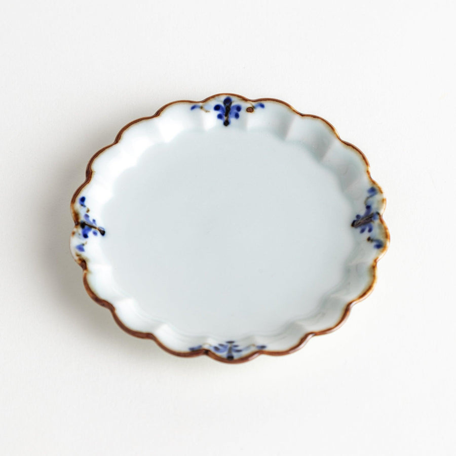 Round white porcelain sauce dish with scalloped edges, adorned with a simple blue floral pattern and brown accent trim.