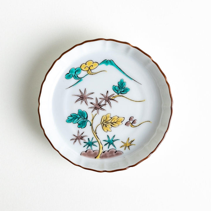 A white ceramic plate with a scalloped edge, decorated with a colorful floral pattern and Mount Fuji in the background.