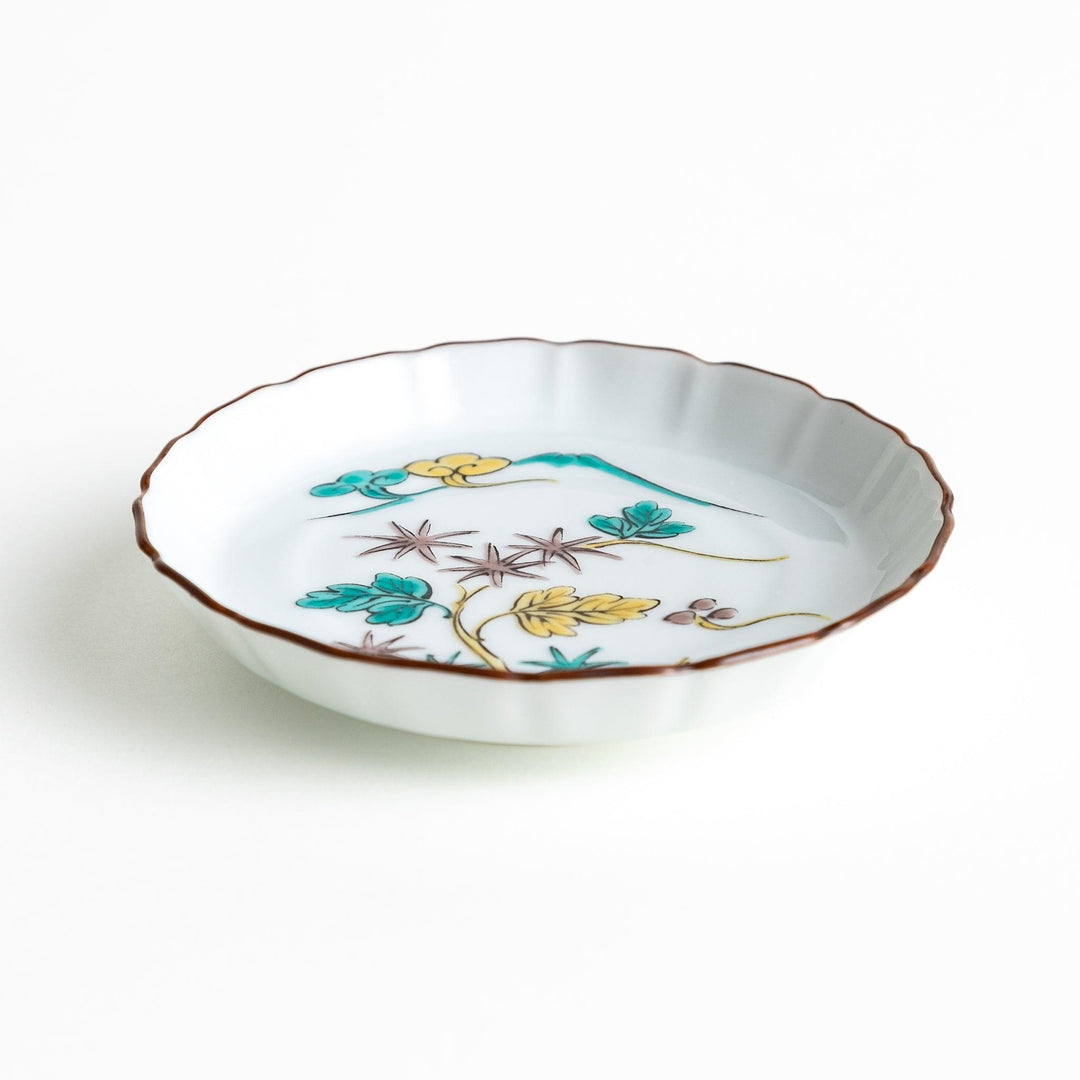 A white ceramic plate with a scalloped edge, decorated with a colorful floral pattern and Mount Fuji in the background.