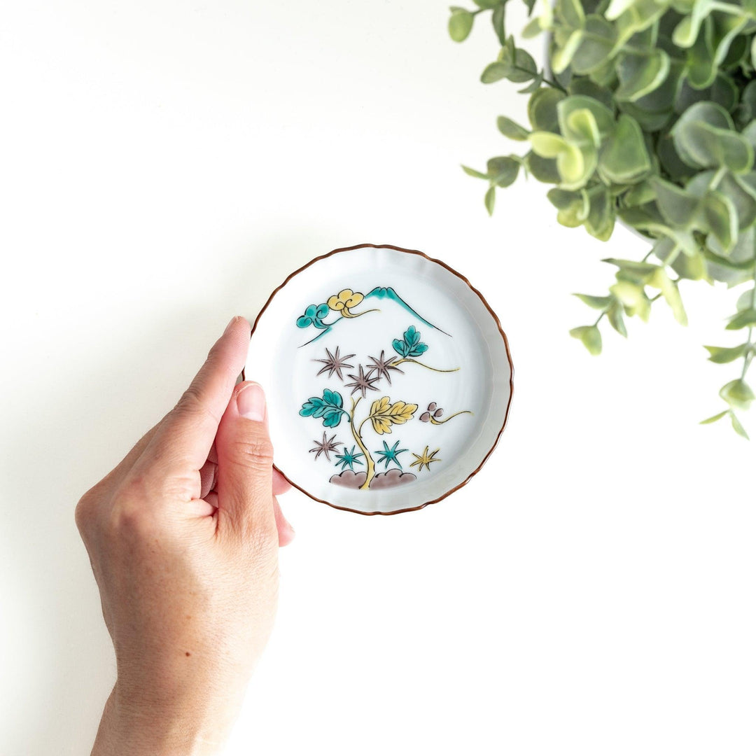 A white ceramic plate with a scalloped edge, decorated with a colorful floral pattern and Mount Fuji in the background.