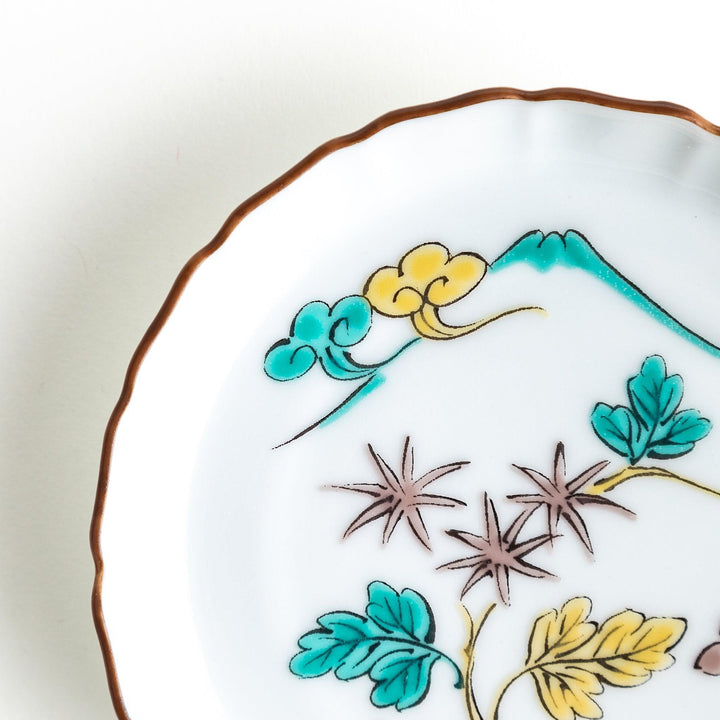 A white ceramic plate with a scalloped edge, decorated with a colorful floral pattern and Mount Fuji in the background.