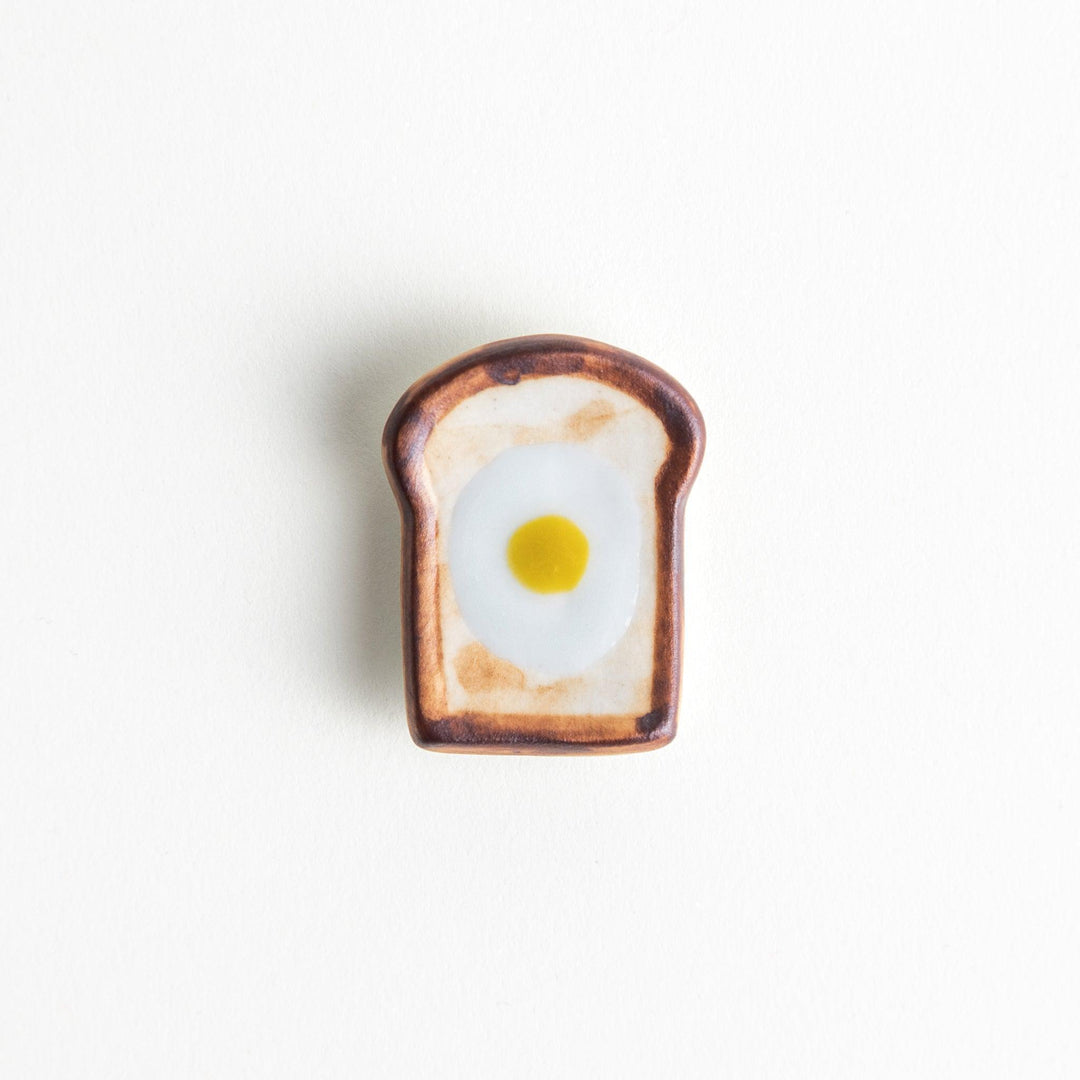 A ceramic chopstick rest resembling a fried egg on toast.