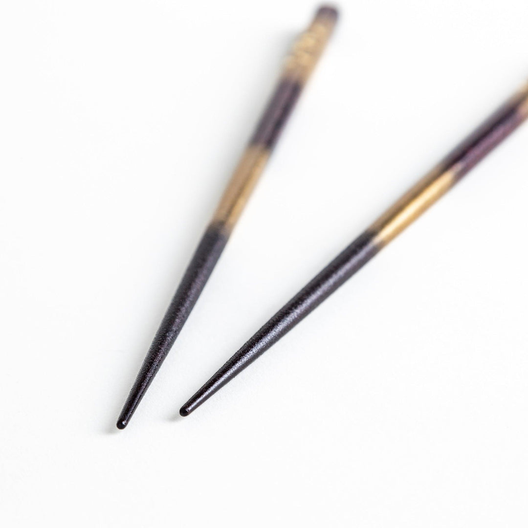 A pair of chopsticks with a gold and silver gradient design.