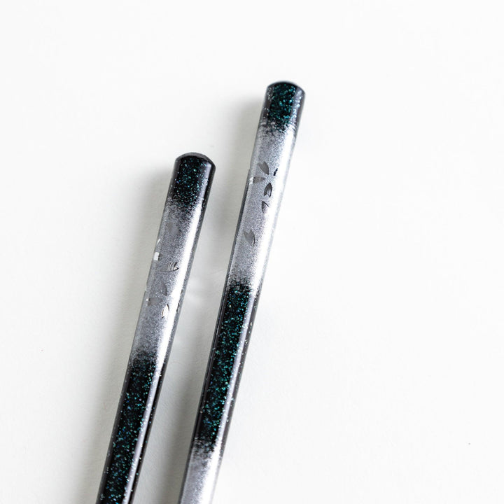 A pair of chopsticks with a gold and silver gradient design.