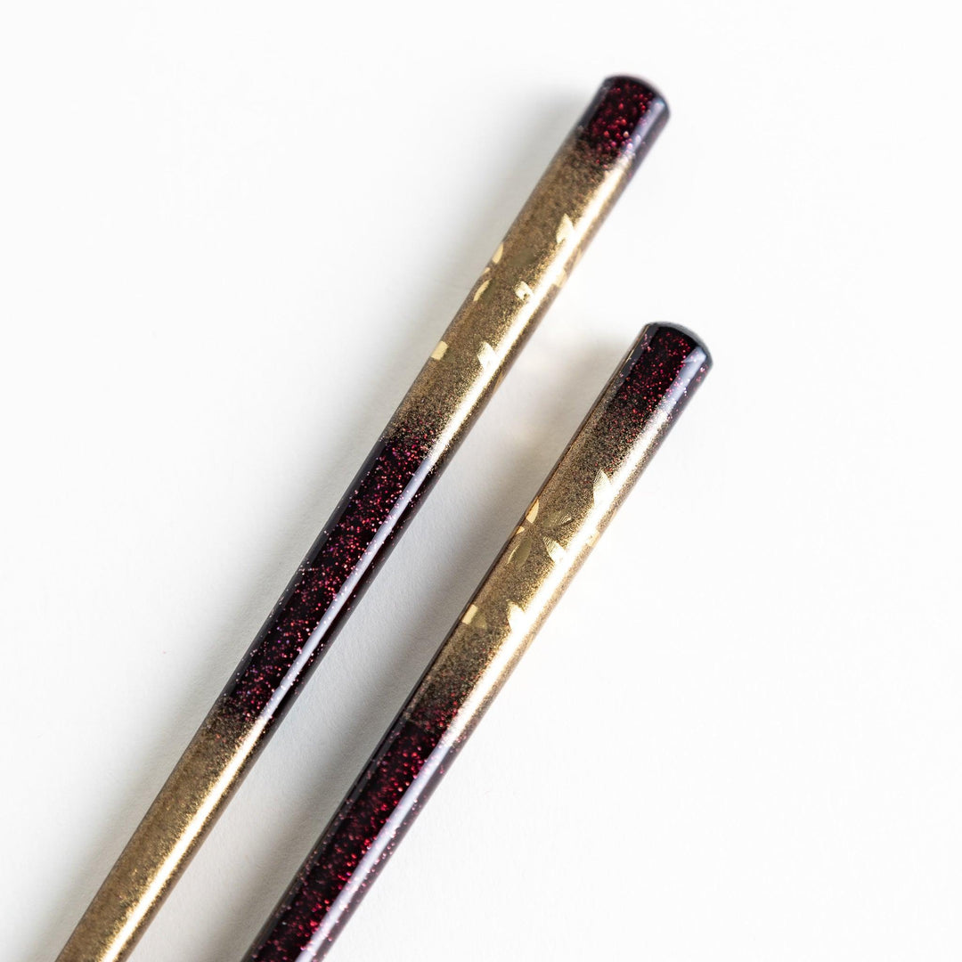 A pair of chopsticks with a gold and silver gradient design.