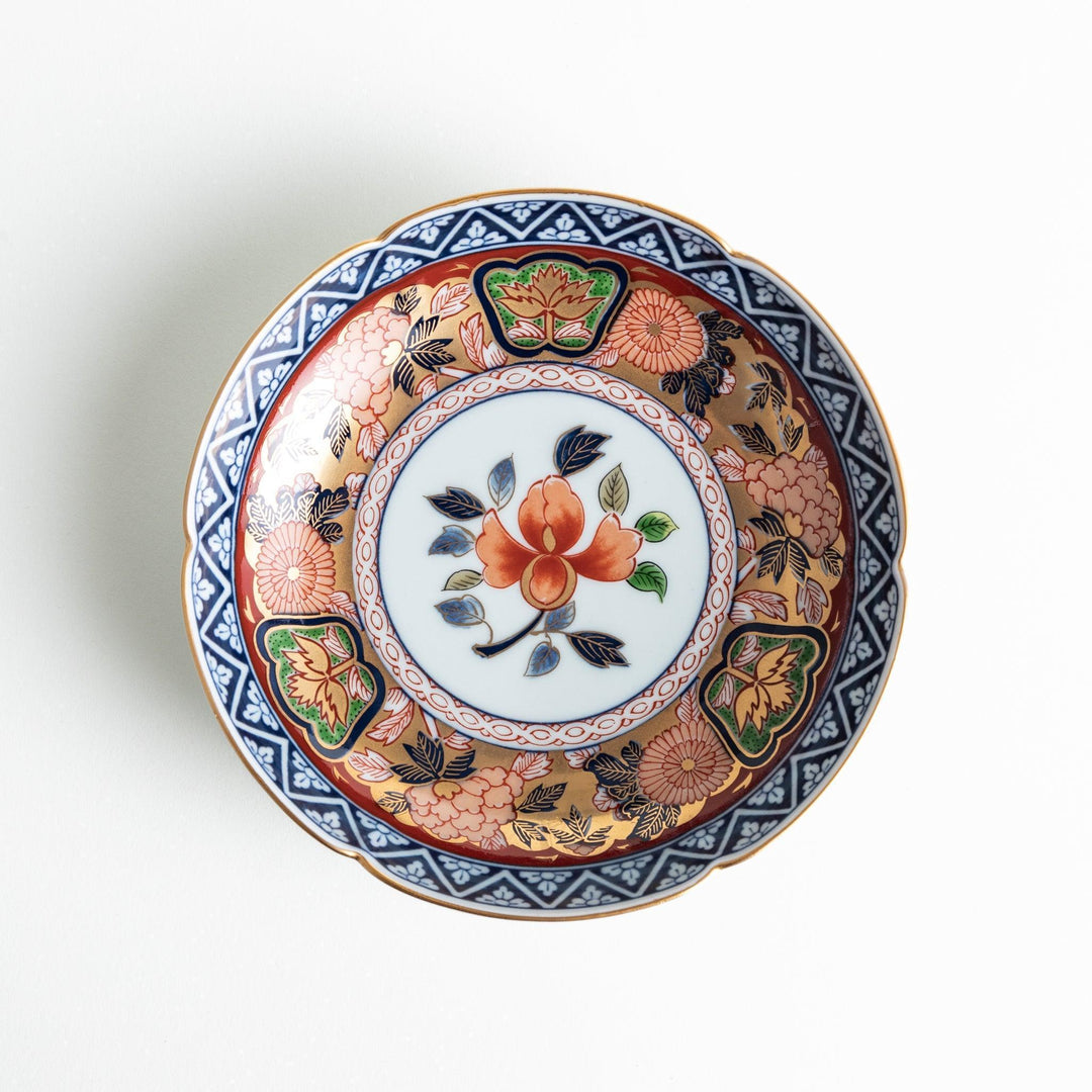 A dessert plate with a central floral design, bordered by intricate multicolored patterns and traditional motifs in gold and blue.