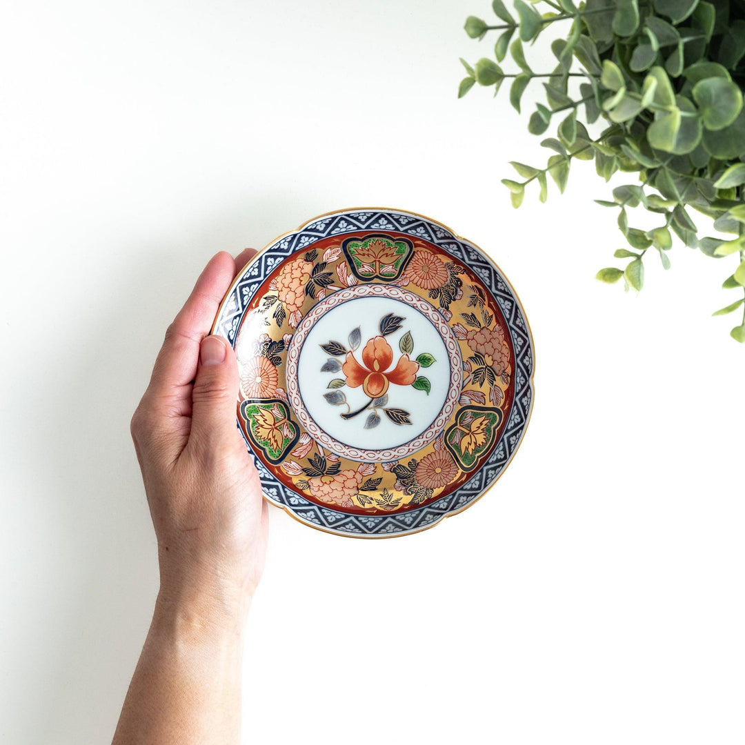 A dessert plate with a central floral design, bordered by intricate multicolored patterns and traditional motifs in gold and blue.