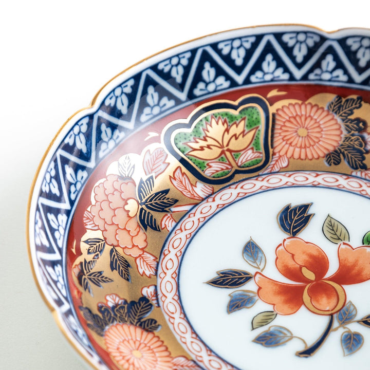 A dessert plate with a central floral design, bordered by intricate multicolored patterns and traditional motifs in gold and blue.