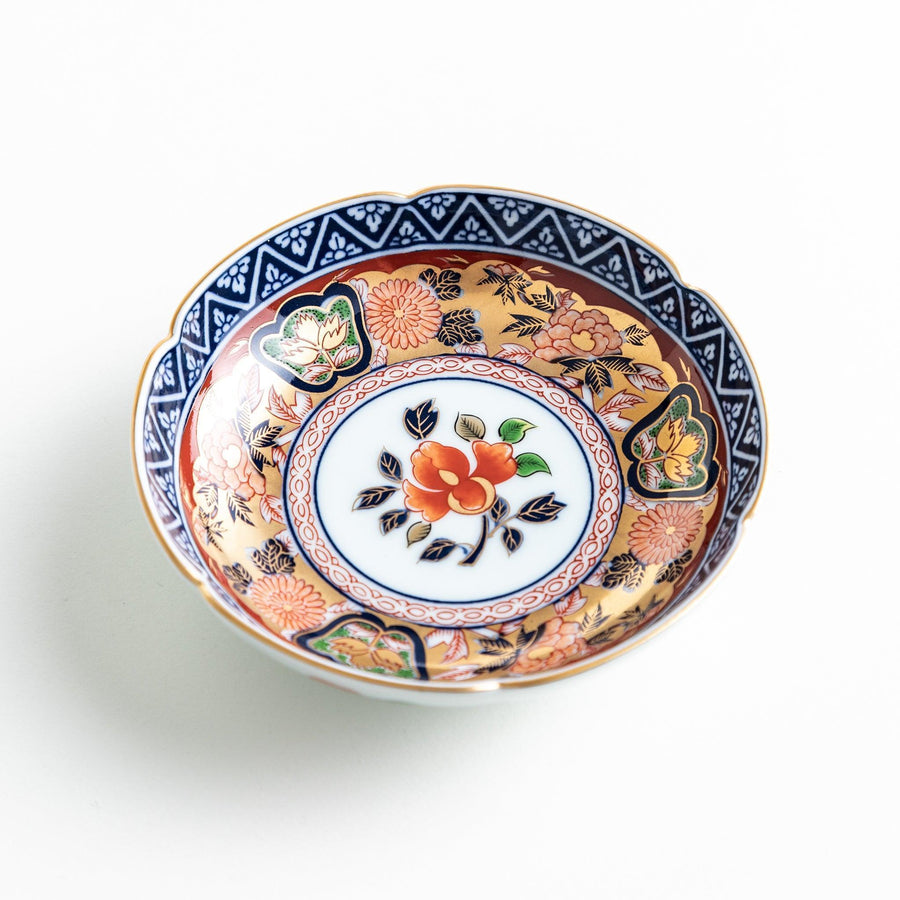 A round sauce dish with a central red floral motif, surrounded by a detailed border of gold, blue, and green floral patterns.