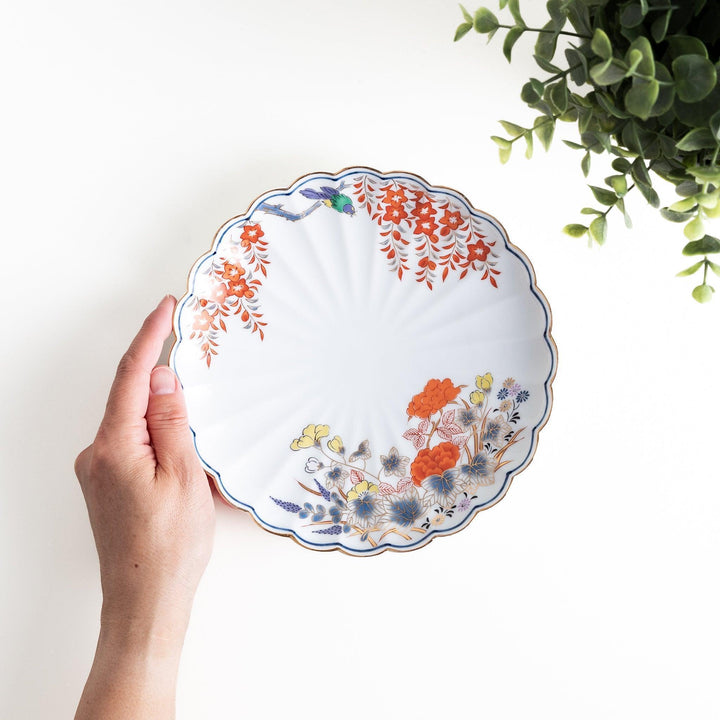 A round salad plate with scalloped edges, featuring delicate floral designs in red, yellow, and blue, with a branch of wisteria hanging from the top.