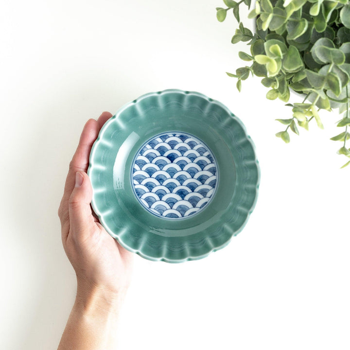 A small green cereal bowl with a scalloped edge and a blue and white wave pattern in the center.