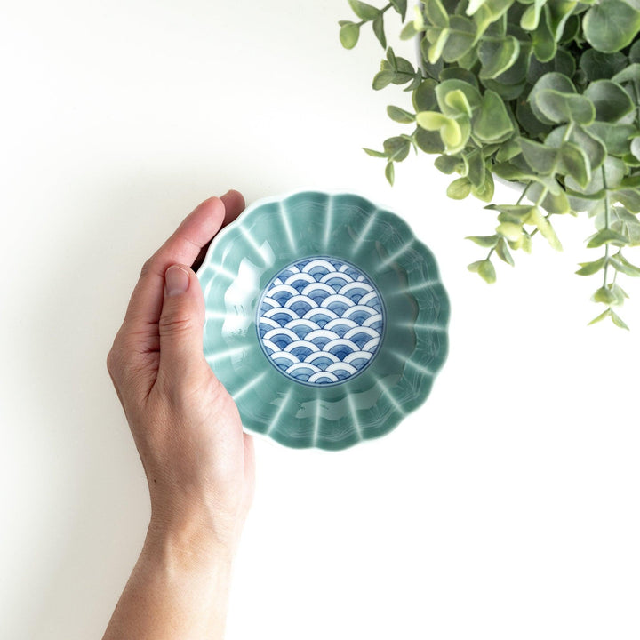 A small green cereal bowl with a scalloped edge and a blue and white wave pattern in the center.