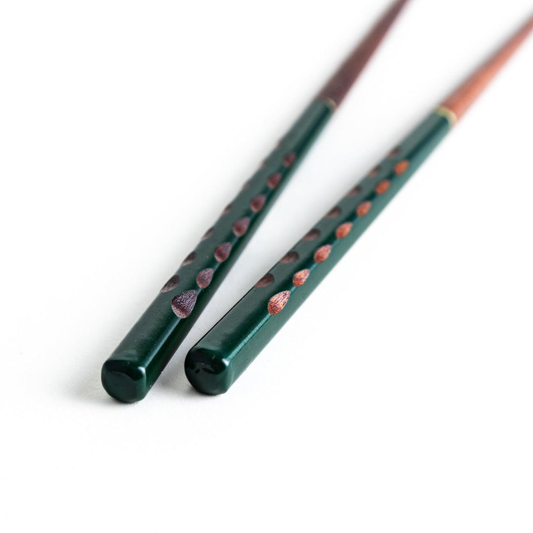 A pair of green-handled chopsticks with a detailed design near the top.