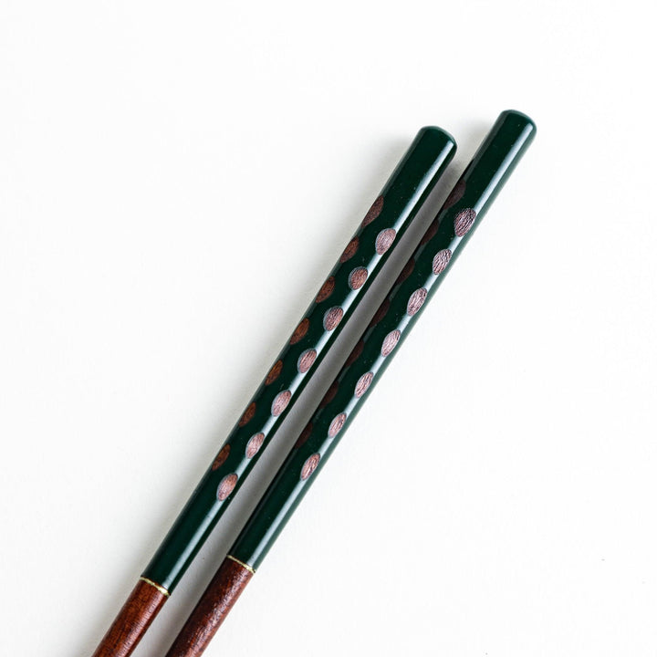 A pair of green-handled chopsticks with a detailed design near the top.