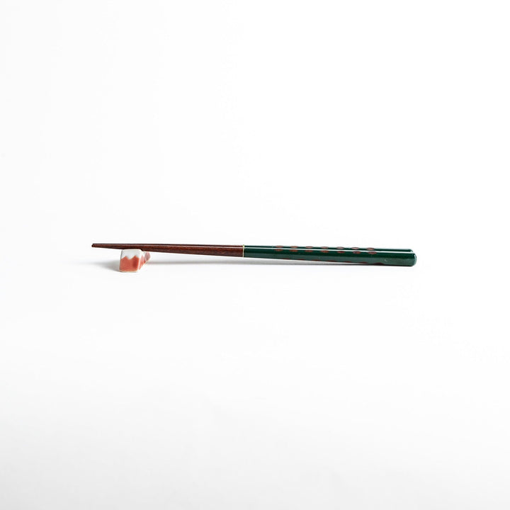 A pair of green-handled chopsticks with a detailed design near the top.