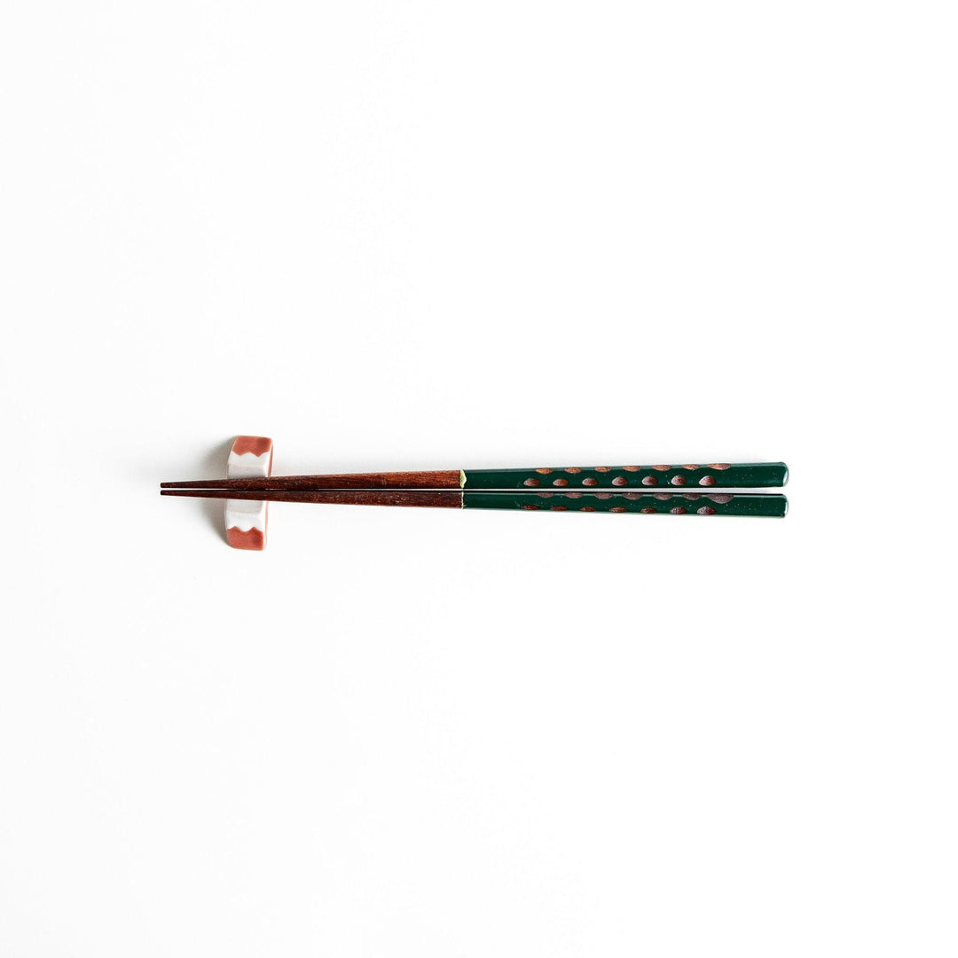 A pair of green-handled chopsticks with a detailed design near the top.