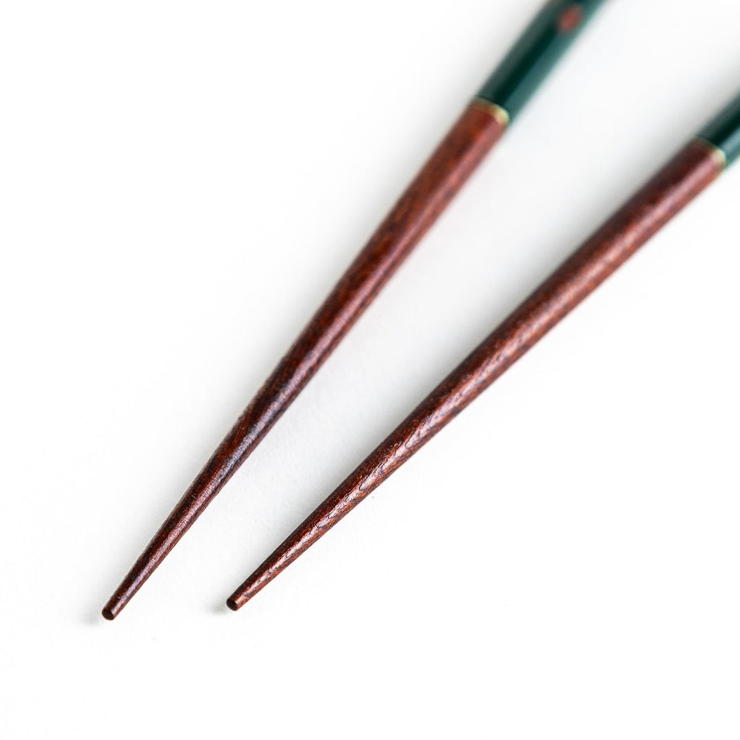 A pair of green-handled chopsticks with a detailed design near the top.