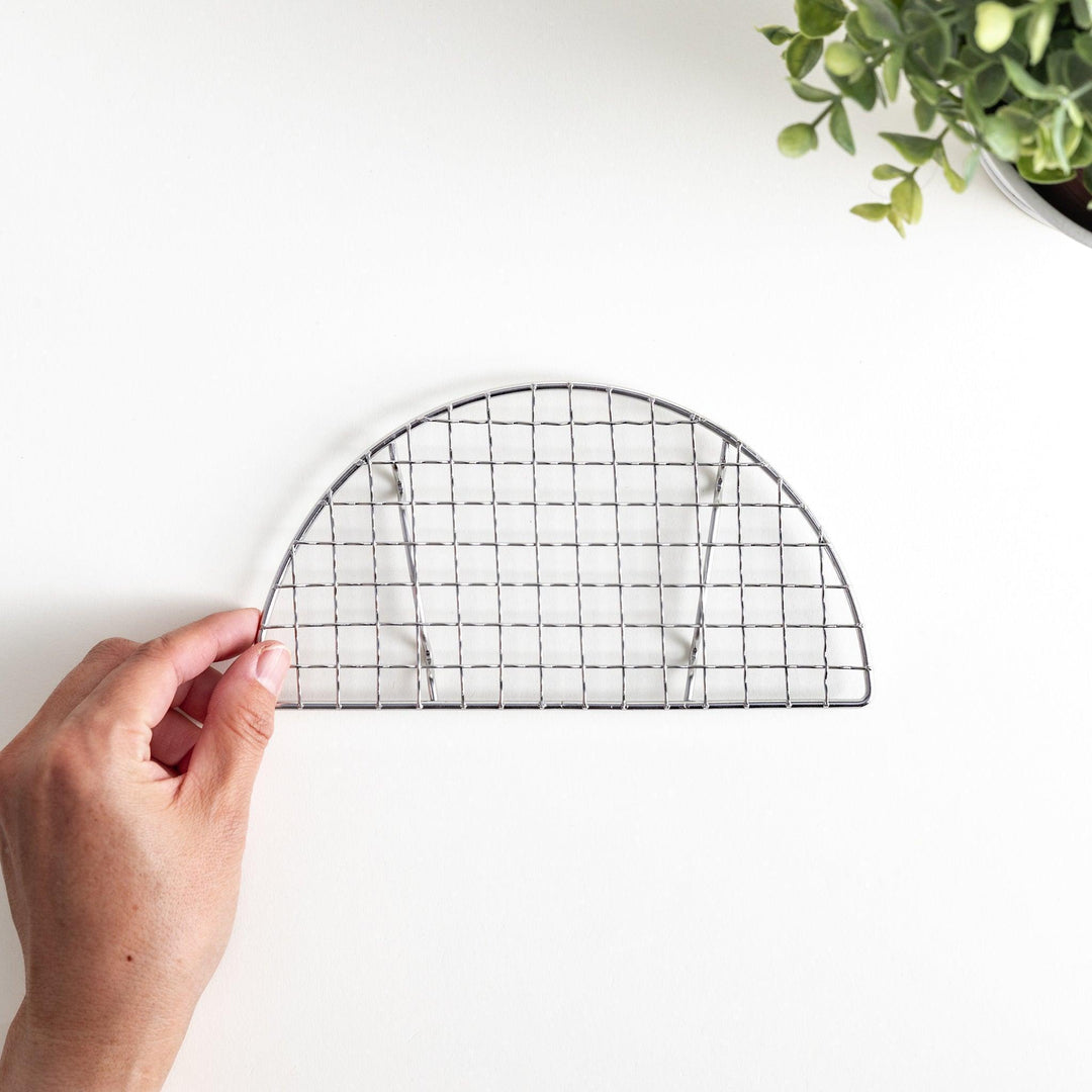 A semi-circular metal grilling rack, featuring a mesh pattern and designed to fit over a heat source for cooking.