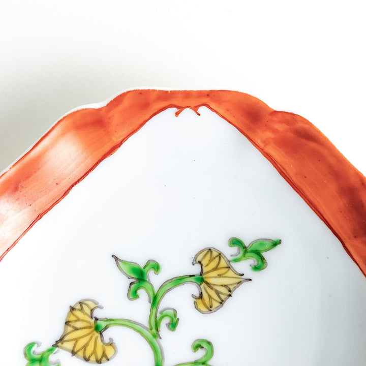 A scalloped Mount Fuji ceramic plate with a red border and an elegant floral design in soft green and yellow tones.