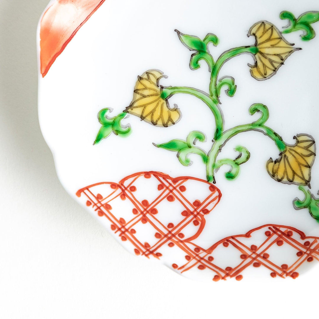 A scalloped Mount Fuji ceramic plate with a red border and an elegant floral design in soft green and yellow tones.