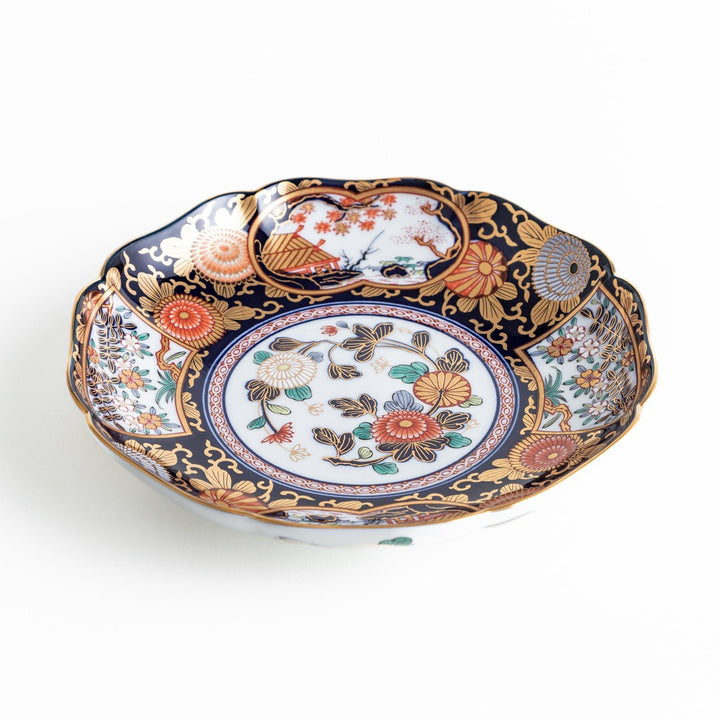 A deep round luncheon plate with a dark blue background, featuring a central floral design and gold accents, surrounded by detailed floral and landscape scenes.